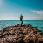 man in black shorts standing on brown rock formation near sea during daytime